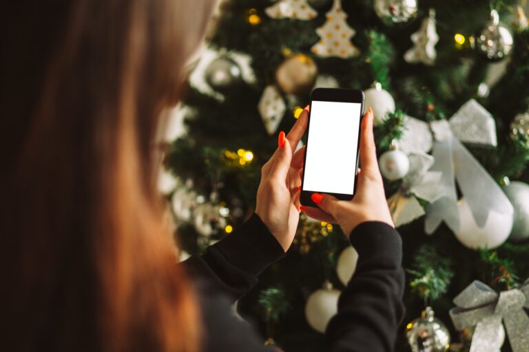 hand holding smart phone mobile near christmas tree